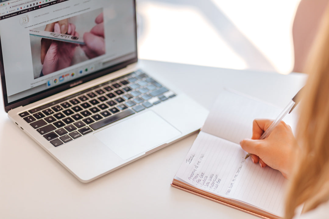 Laptop showing online nail course and girl taking nail theory notes